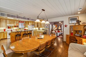 Une cuisine spacieuse avec des meubles en bois, un coin repas doté d’une grande table et de chaises en bois, et un salon confortable avec un canapé et un bureau.