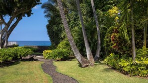 A garden with a winding path, palm trees, and a view of the ocean. - LAST MINUTE DISCOUNT SPECIAL! Central A/C Double Master Suite Home. (Kailua-Kona)