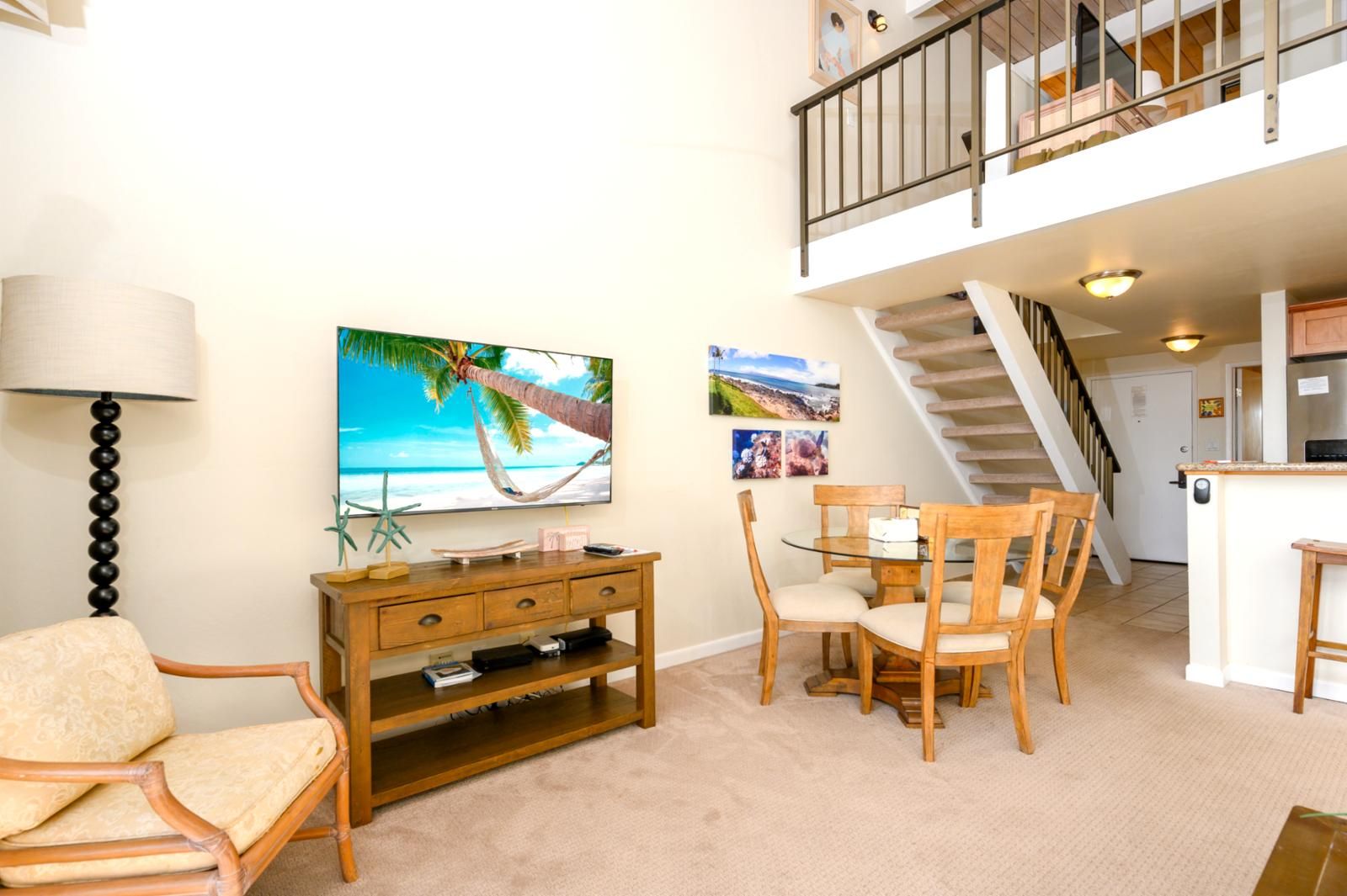 Ein Wohnzimmer mit Fernseher, Holzmöbeln, einem Esstisch und einer Treppe, die zu einer oberen Ebene führt.