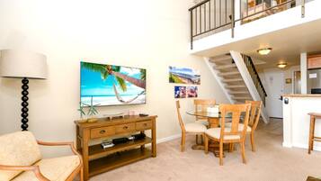 Ein Wohnzimmer mit Fernseher, Holzmöbeln, einem Esstisch und einer Treppe, die zu einer oberen Ebene führt.