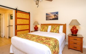 Habitación de hotel con cama, dos lámparas de noche, un cuadro en la pared, una puerta corrediza y un ventilador de techo.
