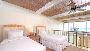 Ein Hotelzimmer mit zwei Betten, einem Deckenventilator, einem Nachttisch mit Lampe und einem Balkon mit Meerblick.
