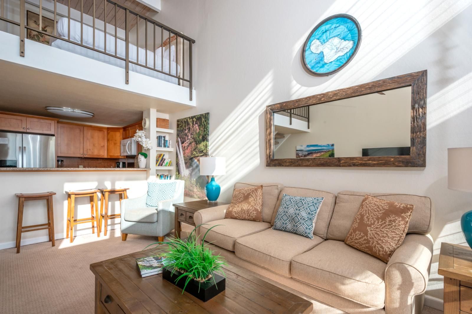 A spacious living area with a high ceiling, a kitchen with wooden cabinets, a large mirror, and a comfortable sofa with cushions.