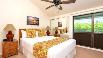 A hotel room with a bed, bedside lamps, a ceiling fan, a large window with a view of greenery, and a mirror.