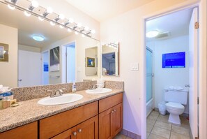 Un baño con dos lavamanos, un espejo grande con iluminación, armarios de madera y un inodoro.