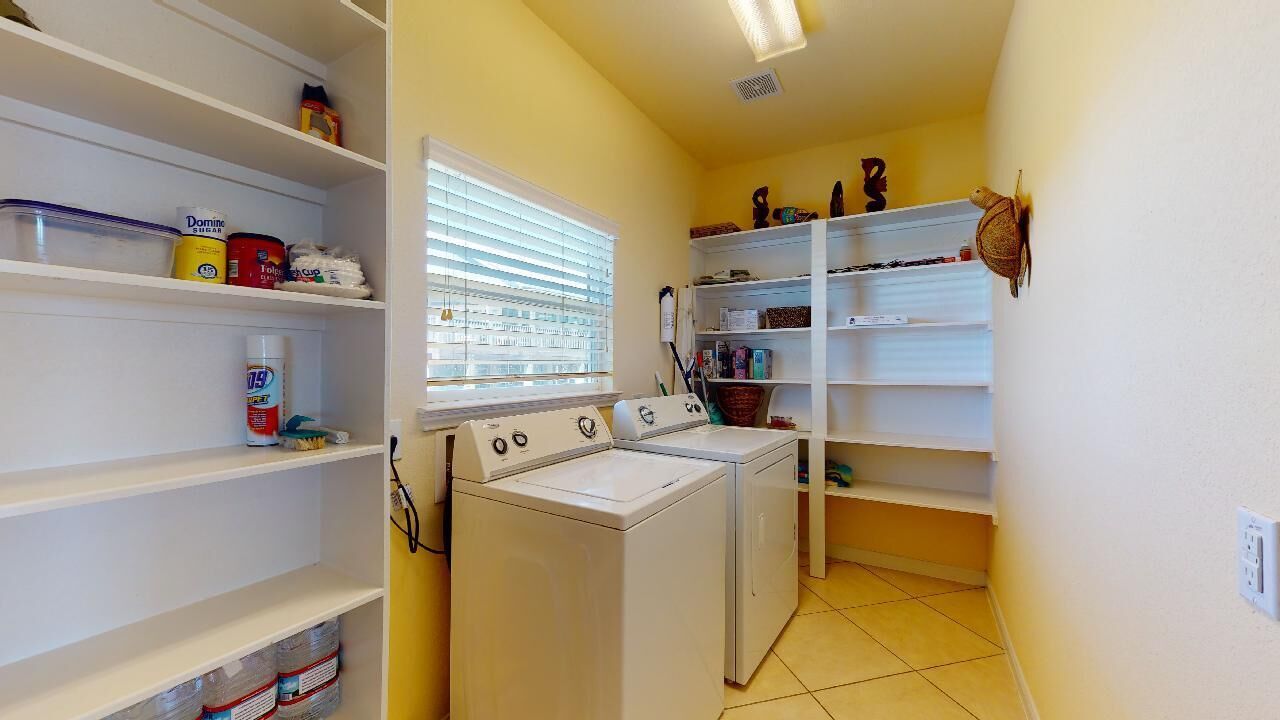 Une buanderie équipée d’un lave-linge, d’étagères contenant des produits de nettoyage et d’une fenêtre avec des stores.