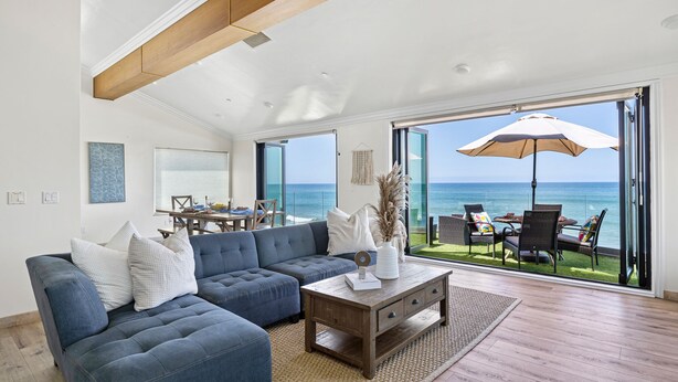 A spacious living room with a large sofa, a coffee table, and a dining area with a view of the ocean. - Beautiful UPPER LEVEL Pet-Friendly Oceanfront Duplex P1111-1 (Oceanside)