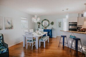 A dining area with a white table set for four, a blue bench, and a kitchen area with a blue countertop and bar stools.