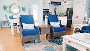 Een woonkamer met twee rieten fauteuils, een glazen salontafel en een blauwe bank.