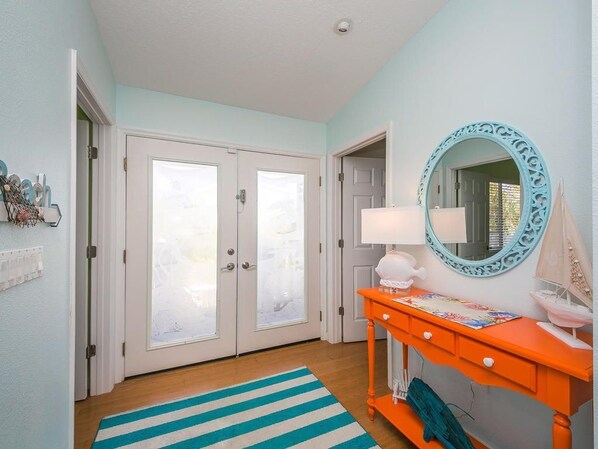 A hallway with a striped rug, a bright orange console table with a lamp, and a decorative mirror. - Tides Inn- Family home with tropical pool area. (Anna Maria)