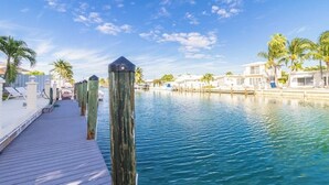 Muelles de madera que conducen a un puerto deportivo con aguas azul cristalino, palmeras y edificios frente a la playa.