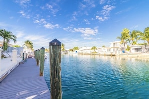 A wooden dock leading to a marina with clear blue water, palm trees, and beachside buildings.