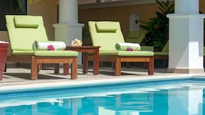 Ein Poolbereich mit zwei grünen Liegestühlen, jeweils mit Handtuch und Blume.