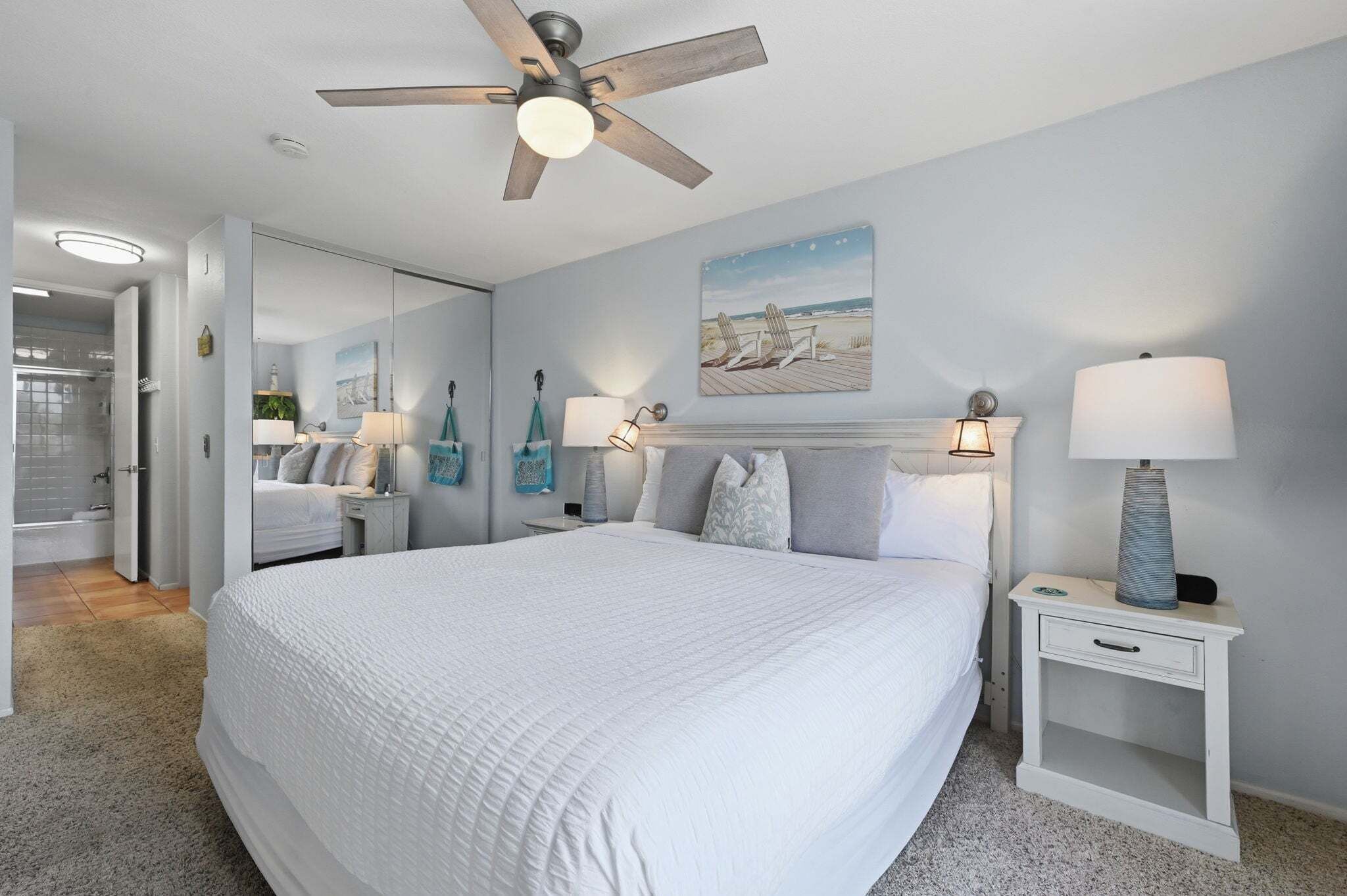 Une chambre à coucher avec un lit, des lampes de chevet, un ventilateur de plafond et un tableau au mur.