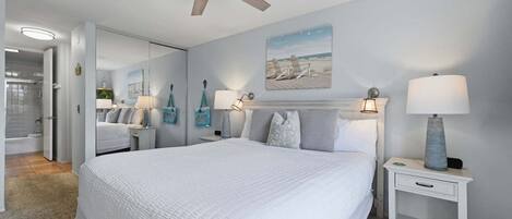 A bedroom with a bed, bedside lamps, a ceiling fan, and a painting on the wall.