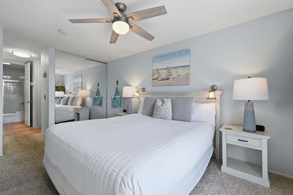 A bedroom with a bed, bedside lamps, a ceiling fan, and a painting on the wall.
