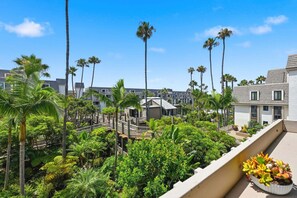A hotel with a rooftop garden, palm trees, and a balcony with potted plants. - Beach Theme Condo with Ocean & Pool View G222 North Coast Village (Oceanside)