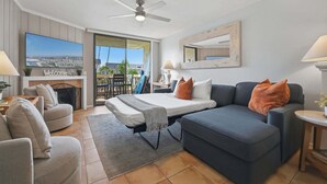 A modern hotel room with a bed, sofa, and armchair, a television, a ceiling fan, and a view of the outdoors.