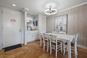 A dining area with a white table and chairs, a ceiling fan, and a painting of pelicans on the wall.