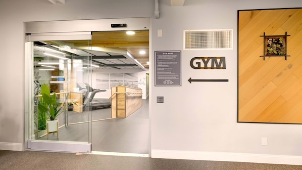A gym entrance with a treadmill, a sign indicating gym rules, and a directional arrow.