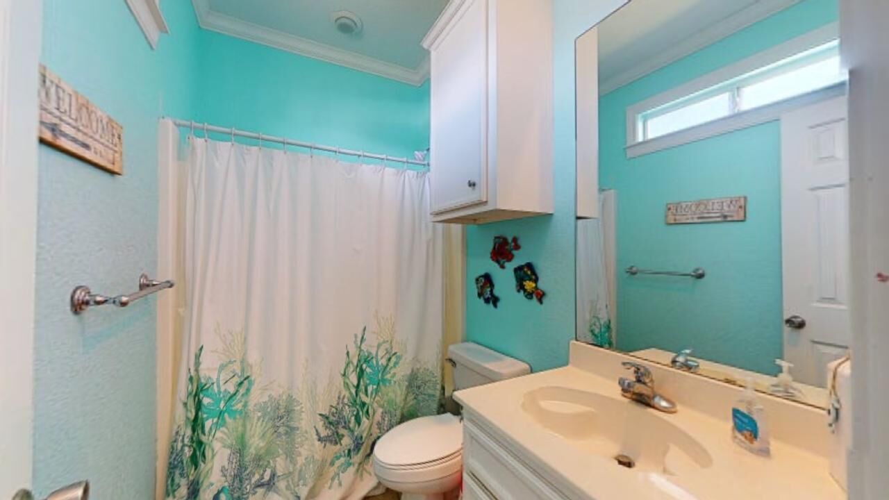 A bathroom with a white toilet, a sink with a mirror, a shower curtain, and a wall with a sign.