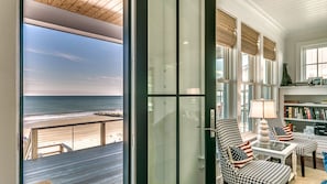 Una stanza con vista sulla spiaggia, una porta vetrata, una poltrona a motivi a zig-zag, una lampada e una libreria.