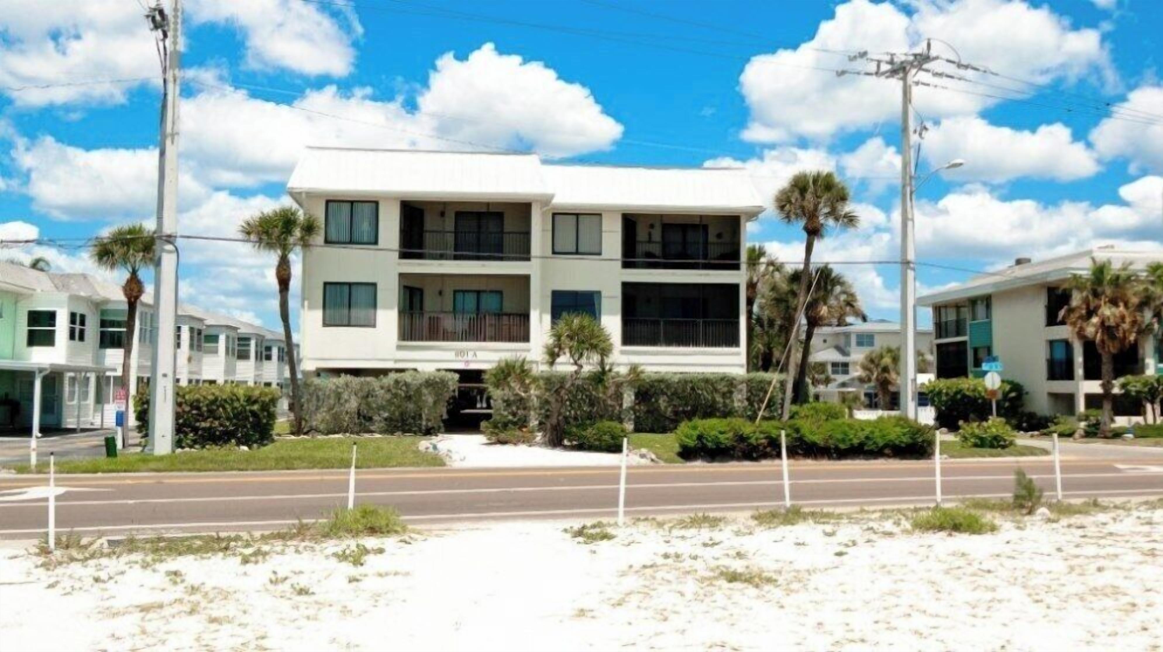 A two-story hotel with a flat roof, multiple balconies, and a well-maintained front lawn with palm trees.