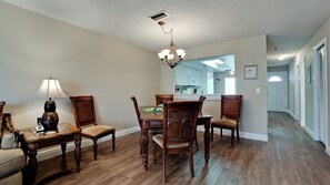 A dining area with a wooden table and chairs, a chandelier, and a lamp. - Gulf Watch 205 - Anna Maria Island - Condo 2 Bedroom / 2 Bath Gulf to Bay access, maximum occupancy of 4 people. (Bradenton Beach)
