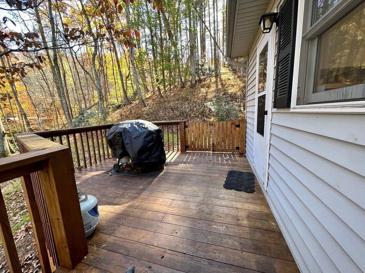A wooden deck with a barbecue grill and a covered grill, surrounded by trees.