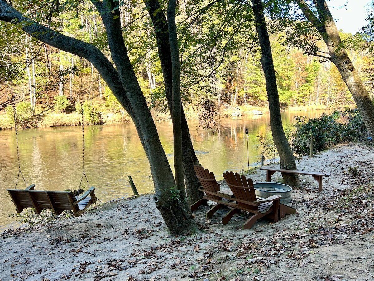 A lakeside campsite with a swing, Adirondack chairs, and a picnic table.