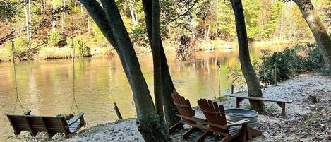 A lakeside campsite with a swing, Adirondack chairs, and a picnic table.
