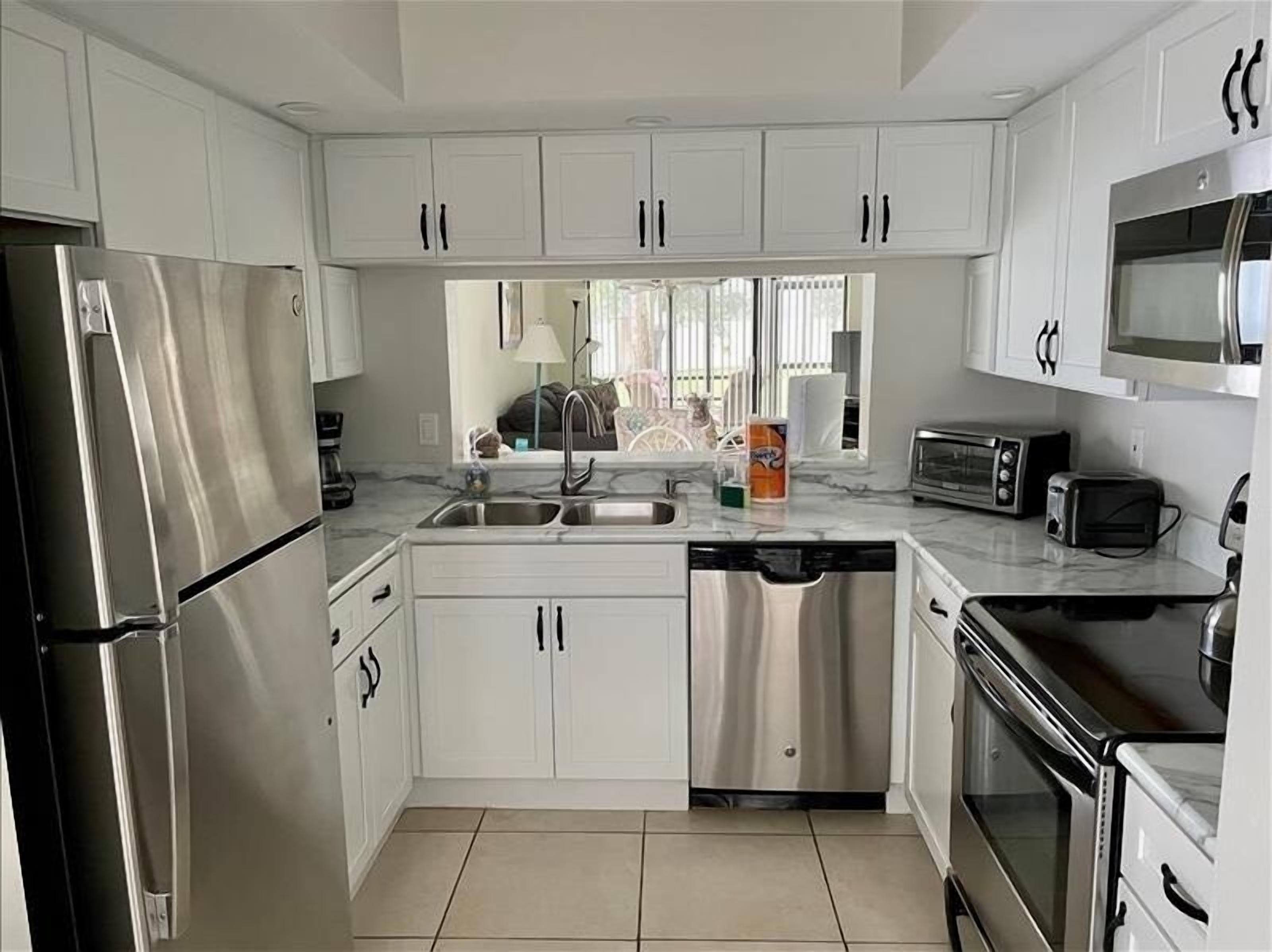 A modern kitchen with white cabinets, stainless steel appliances, and a tiled floor.
