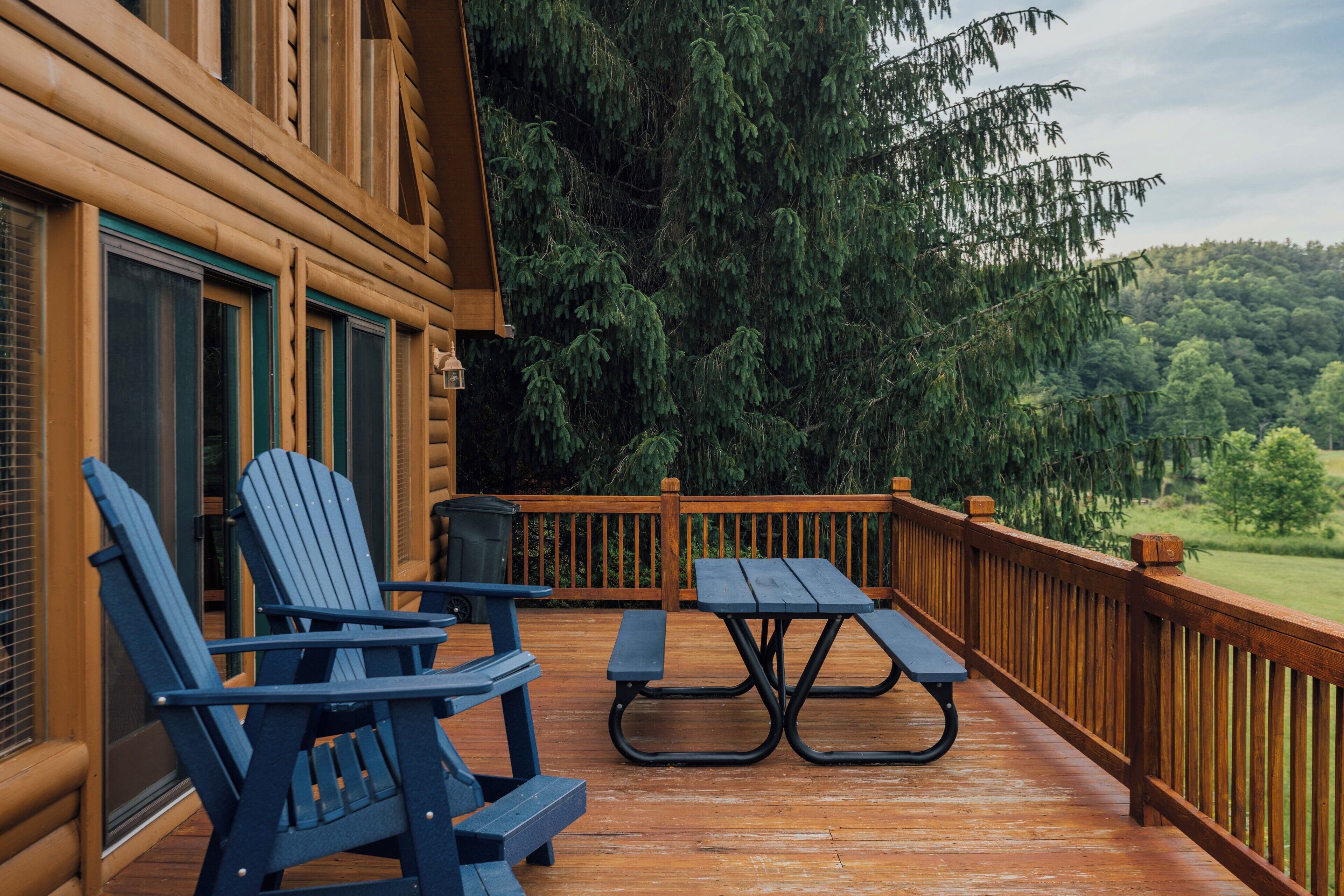 Terraza de madera con sillas Adirondack y una mesa de picnic, rodeada por una barandilla de madera y un bosque denso.