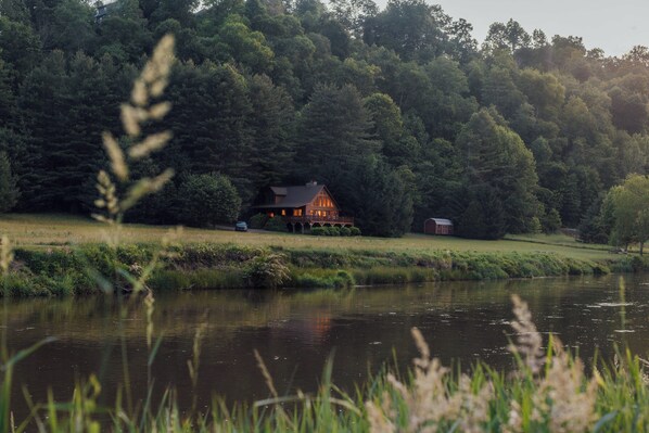 A cabin by a lake with a deck and a red barn in the background.
