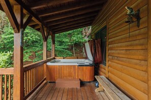 A wooden deck with a hot tub, wooden railings, and a view of a forested area.