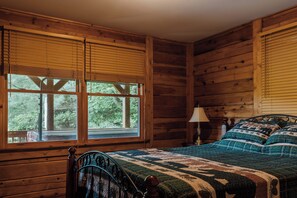 Una habitación de cabaña de madera con una cama, una mesita de noche y una ventana con persianas.