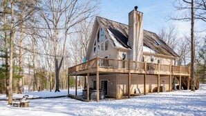 A wooden cabin with a deck, surrounded by snow and trees. - Peaceful Dog Friendly Escape w/ Dock & Fire Pit (Swanton)
