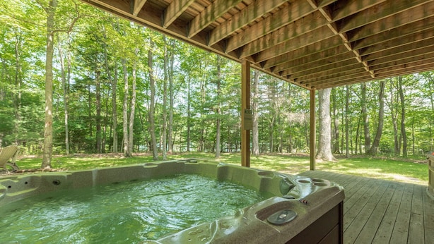 A hot tub under a wooden deck surrounded by a forest. - Peaceful Dog Friendly Escape w/ Dock & Fire Pit (Swanton)
