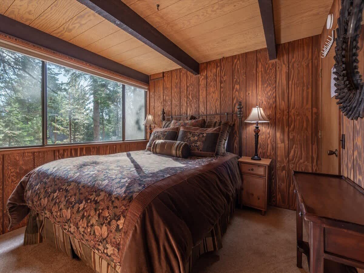 Ein Schlafzimmer mit einem großen Bett, Holzwänden, einem Fenster mit Blick auf einen Wald und einem Nachttisch mit einer Lampe.