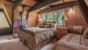 A bedroom with a loft-style ceiling, a bed with a patterned bedspread, a nightstand with a lamp, and a window with a view of trees. - Unique 3 Story with Two Great Entertainment Areas! Short drive to Lake and Northstar! (Kings Beach)