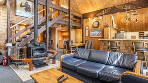 A cozy cabin interior with a wooden staircase, a leather sofa, a kitchen area, and a fireplace. - Chalet #4, Slope Side Ski in Ski Out Spacious Fami (Mammoth Lakes)