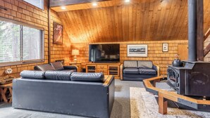 A cozy cabin interior with a fireplace, wooden walls, a sofa, and a television. - Chalet #4, Slope Side Ski in Ski Out Spacious Fami (Mammoth Lakes)