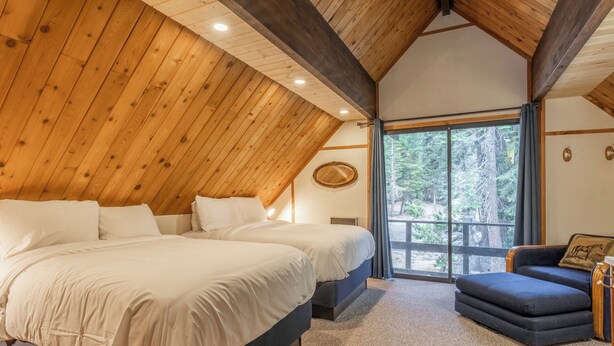 A bedroom with a large bed, a small sofa, and a window with a view of trees. - Chalet #4, Slope Side Ski in Ski Out Spacious Fami (Mammoth Lakes)