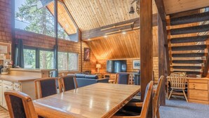 A cozy cabin interior with a wooden dining table, chairs, a sofa, and a television. - Chalet #4, Slope Side Ski in Ski Out Spacious Fami (Mammoth Lakes)