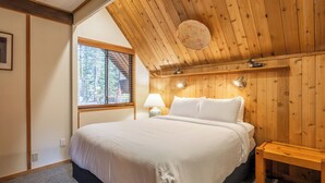 A bedroom with a wooden ceiling, a bed with white bedding, a bedside lamp, and a window with blinds. - Chalet #4, Slope Side Ski in Ski Out Spacious Fami (Mammoth Lakes)