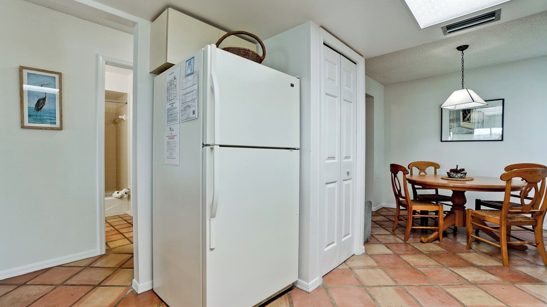 Una cocina compacta con un refrigerador blanco, una mesa de comedor con cuatro sillas y piso de baldosas.