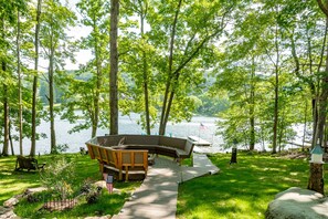 A lakeside deck with a curved bench and a small American flag, surrounded by lush greenery and a view of the lake.