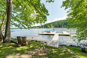 A lakeside dock with chairs and a flag, surrounded by trees and a grassy area.
