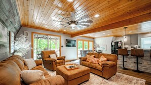 A spacious living area with leather sofas, a wooden ceiling, and a kitchen in the background. - Dog Friendly Getaway Just Steps to Wisp & Fun (MCHENRY)