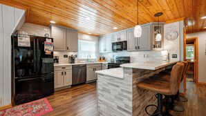 A modern kitchen with wooden ceiling, stainless steel appliances, and a bar area. - Dog Friendly Getaway Just Steps to Wisp & Fun (MCHENRY)